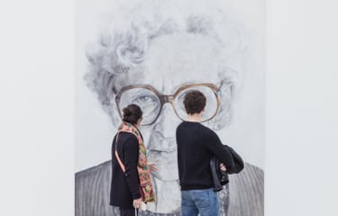 Man and Woman looking
          at a photograph gallery piece of an senior woman black and white
          wearing brown glasses.